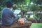 The young man was reading a book at the park. Among the natural trees and beautiful flower garden