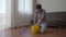 A young man washes floor in an apartment. He puts washing liquid into the bucket. Cleaning service concept. Gender