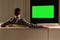 A young man is watching TV with a green screen