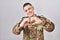 Young man wearing camouflage army uniform smiling in love doing heart symbol shape with hands