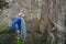 Young man wearing in climbing equipment with rope standing in front of a stone rock and preparing to climb