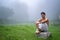 Young man wearing a dhoti, sitting on a rock, open in the green field in a foggy morning