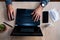 Young man wearing medical face mask at work from home due to corona virus outbreak with laptop and mobile phone on wooden table,