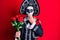 Young man wearing mexican day of the dead costume holding roses covering mouth with hand, shocked and afraid for mistake