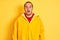 Young man wearing rain coat standing over isolated yellow background afraid and shocked with surprise expression, fear and excited