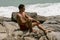 A young man wearing red swimming shorts sitting on the rocks and looking to ocean. Summer resting on the beach.