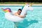 Young man wearing sunglasses hugging a big unicorn inflatable ring in a pool.