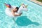 Young man wearing sunglasses hugging a big unicorn inflatable ring in a swimming pool
