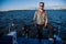 Young man wearing sunglasses standing on yacht stern and enjoying perfect autumn day under sails - sailing holidays