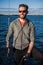 Young man wearing sunglasses standing on yacht stern and enjoying perfect autumn day under sails - sailing holidays