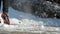 Young man wearing warm trousers and black sneakers is playing with snow by kicking snowdrift in city park on sunny winter day