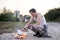 Young man, wearing white t-shirt and grey pants and bracelets, burning bonfire of paper on abandoned construction area industrial