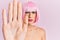 Young man wearing woman make up wearing pink wig doing stop sing with palm of the hand