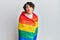 Young man wearing woman make up wrapped in rainbow lgbtq flag looking at the camera blowing a kiss being lovely and sexy