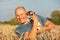 Young man in wheat field, afternoon light, holding Jack Russell terrier puppy on hands, moving head away, making a grimace,