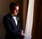 young man in a white shirt fastens cufflinks on sleeves near the window. business portrait. The groom is going to meet the bride.