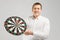 Young man in white shirt holding a target with Darts in center isolated on white background