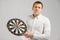 Young man in white shirt holding a target with Darts in center isolated on white background