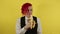 Young man in white shirt, vest and tie eating banana on yellow background in studio. Businessman biting yummy fruit