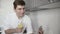 Young man in a white short uses reusable eco-friendly ecological bamboo straw to drink water with lemon at the kitchen