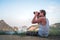 A young man in a white T-shirt sits on the top and looks into the distance through binoculars at a beautiful seascape and rocks