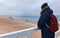 A young man in winter in a jacket, a hat and a backpack stands on the pier and looks at the Baltic Sea