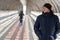 A young man in a winter jacket stands in a light tunnel and looks away. Profile view of handsome young man outdoor, looking away