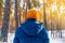 Young man in winter yellow hat walks in winter snowy pine forest