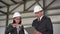 Young man and woman in helmets with documents at a construction site. Businessmen in suits measure the detail with a