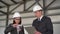 Young man and woman in helmets with documents at a construction site. Businessmen in suits measure the detail with a