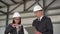 Young man and woman in helmets with documents at a construction site. Businessmen in suits measure the detail with a