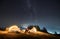 Young man and woman hikers sitting on grassy hill under night starry sky.