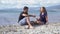 Young man and woman relax sitting by sea on sunny day. Media. Man and woman drink wine from glasses sitting on beach