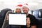 Young man and woman in santa claus hats holding digital tablet in cabin of airplane