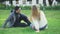 Young man and woman sit on grass in park and laugh. Media. Beautiful couple relax and laugh sitting on green grass