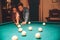 Young man and woman stand together in billiard room. He teach her how to aim into billiard ball. They dating.