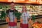 Young man and woman stand at vegetable basket in grocery store. They hold good healthy carrot in hands. Workers pose and