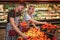 Young man and woman stand at vegetables basket in grocery store. They put peppers together and smile. Hardworking people