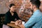 Young man and woman talking about something serious while sitting at a table in a cafe on the background of a rough brick wall