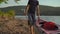 A young man and woman tourists carrying a big inflatable kayak by a seashore or a lake