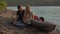 A young man and woman tourists sitting by a big inflatable kayak on a seashore or a lake