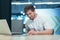 A young man at work is sick, working on a laptop holding his hands to his chest and abdomen