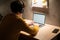 Young man working on laptop in home office. Male student studying in university dormitory at night, typing on laptop