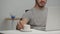 Young man is working at laptop in office room, drinking his coffee, typing on his computer.