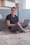 Young man working on laptop sitting on carpet in living room