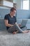 Young man working on laptop sitting on carpet in living room