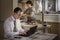 Young man works at a computer at home on the background of a woman busy cooking.