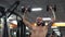 Young man works out in the gym serious focused shakes his arms, pushes the barbell