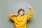 Young man in yellow clothes is dancing on a background of a gray wall in wireless headphones listening to music