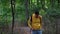 Young man in yellow hoodie with backpack and map walking in woods. Male tourist throws out map, takes out smartphone and